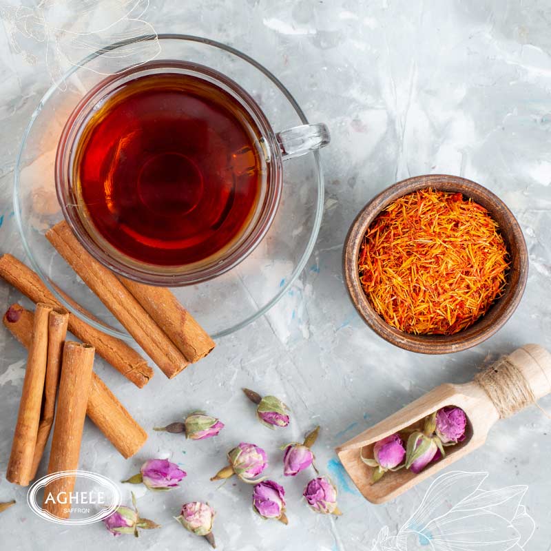 دم کردن زعفران-چای زعفرانی در لیوان شیشه ای که کنار آن دارچین و گل محمدی است3