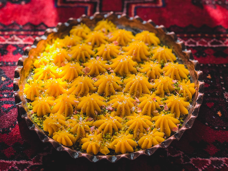 حلوا زعفرانی در سینی مسی روی قالی ایرانی که در نور آفتاب است.