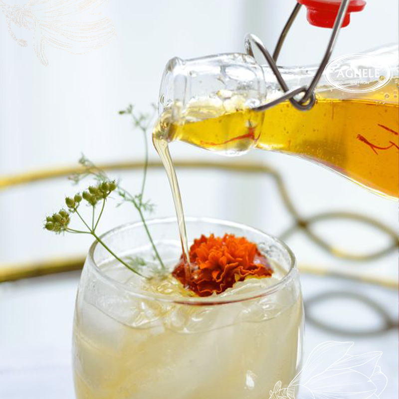 شربت زعفرانی در حال ریخته شدن در لیوان که یک گل نارنجی روی سطح آن است.