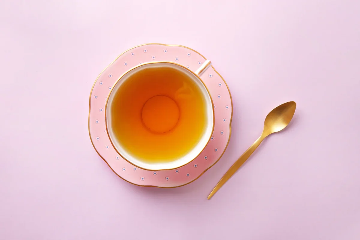 چای زعفران در فنجان صورتی که یک قاشق طلایی کنار آن است